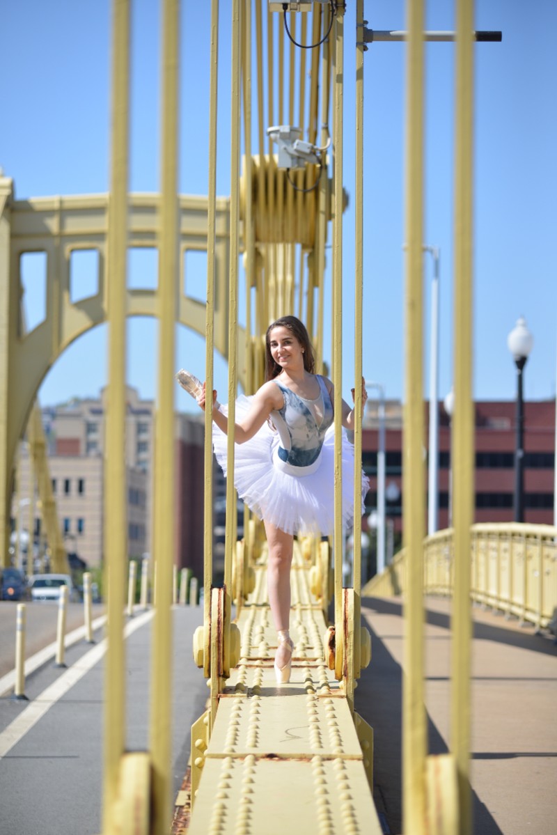 In the image, Katja is wearing a ballet outfit and dancing between poles on a yellow bridge.